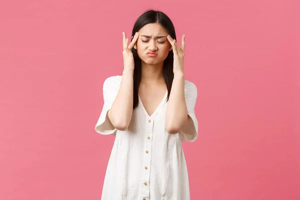 Belleza, emociones de la gente y el ocio de verano y el concepto de vacaciones. Mujer asiática angustiada tocando las sienes y haciendo muecas con los ojos cerrados de la migraña, dolor de cabeza, fondo rosa — Foto de Stock