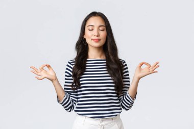 Yaşam tarzı, insanların duyguları ve gelişigüzel kavramlar. Sakin ve sabırlı gülümseyen, gözleri kapalı Asyalı bir kadın sakinleşmek için meditasyon yapıyor, elleri zen hareketiyle nefes egzersizleri yapıyor.