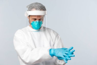 Covid-19, virüs, sağlık çalışanları ve aşı konsepti. Korunma ekipmanındaki doktor, Coronavirus hastalığı olan insanlarla hasta koğuşuna girmeden önce lastik eldiven giydi.