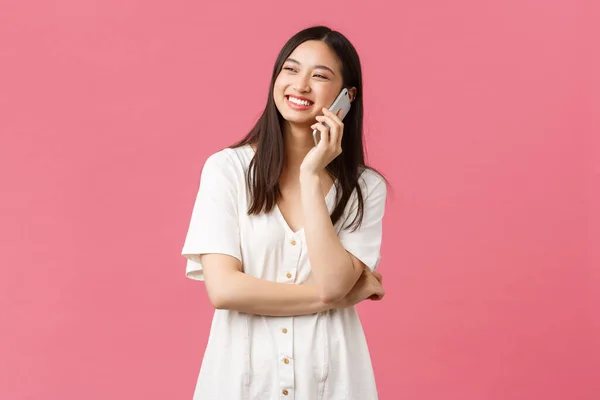 Belleza, emociones de la gente y concepto de tecnología. Amistosa chica bonita sonriente en vestido blanco hablando por teléfono feliz, mirando hacia arriba y de pie fondo rosa alegre —  Fotos de Stock