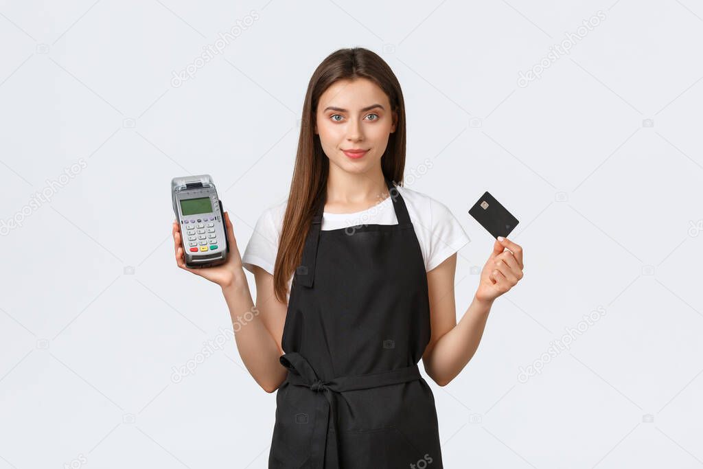 Grocery store employees, small business and coffee shops concept. Friendly cute cashier, saleswoman in black apron showing credit card and POS terminal, easy contactless payment in shop