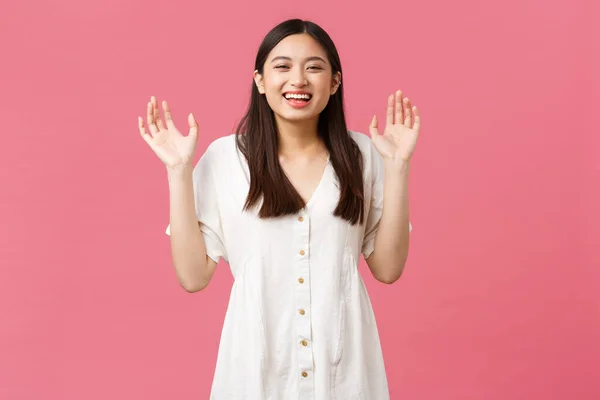 Краса, емоції людей та концепція літнього дозвілля. Щаслива усміхнена азіатська дівчина сміється і показує порожні руки, піднімає руки і гітари, розважається над рожевим тлом — стокове фото