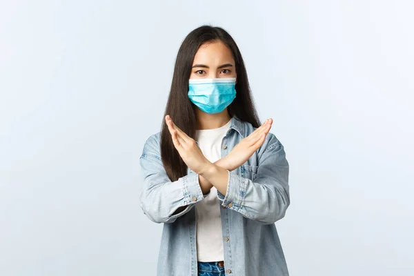 Social distanslivsstil, covid-19 pandemisk vardag och fritidskoncept. Allvarligt missnöjd asiatisk flicka i medicinsk mask visar kors tecken, ogilla eller förbjuda något, berätta att sluta — Stockfoto