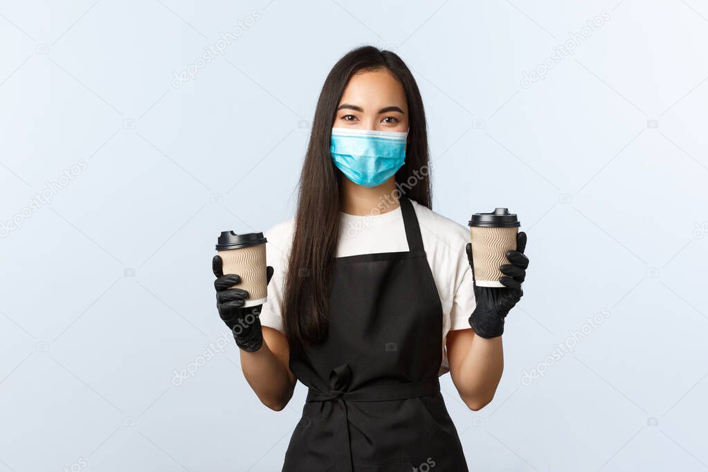 Covid-19, social distancing, small coffee shop business and preventing virus concept. Smiling cute asian cafe owner, employee in medical mask and gloves serving coffee in takeaway cups