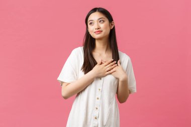 Güzellik, insan duyguları ve yaz tatili konsepti. Beyaz elbiseli, hayalperest ve romantik Asyalı kız arkadaş. Mükemmel randevuyu görüntülüyor. Kalbe dokunan el ele tutuşuyor, pembe arka plan.