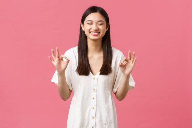 Güzellik, insanların duyguları, yaz tatili ve tatil konsepti. Mutlu, neşeli, sevimli Asyalı gülümseyen kız. Gözleri kapalı gülüyor ve tamam işareti gösteriyor. Sevilen ürün, pembe arka plan.