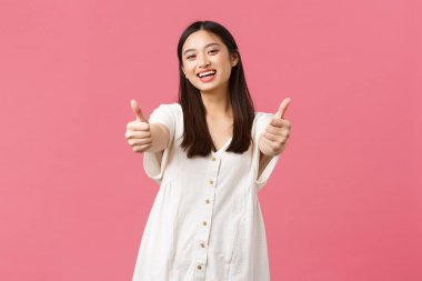 Güzellik, insanların duyguları, yaz tatili ve tatil konsepti. Dost canlısı Asyalı kız gülümsemesi ve baş parmak işareti, harika bir otel ya da spa merkezi tavsiye etmek, pembe arka plan