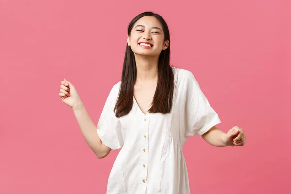 Belleza, emociones de la gente y concepto de ocio de verano. Despreocupado atractiva chica coreana feliz en vestido blanco bailando y riendo de la felicidad, de pie fondo rosa —  Fotos de Stock