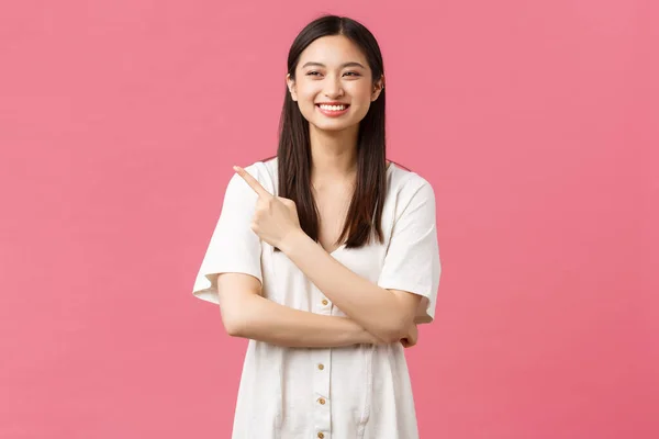Szépség, emberek érzelmei és nyári szabadidő koncepció. Vonzó boldog ázsiai lány aranyos ruha, mutató ujj bal felső sarokban, és nevet, mint a reklám termék vagy bevásárlóközpont promo ajánlat — Stock Fotó