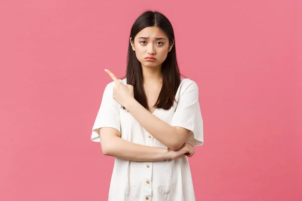 Belleza, emociones de la gente y concepto de ocio de verano. Niña triste trastornada en vestido blanco, enfurruñada y frunciendo el ceño como apuntando esquina superior izquierda a malas noticias, decepcionante anuncio de banner —  Fotos de Stock