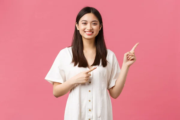 Bellezza, emozioni delle persone e il tempo libero estivo e concetto di vacanza. Bello sciocco ragazza asiatica in abito bianco raccomandare visita negozio o fare clic sul link, sorridente fotocamera e puntando a destra — Foto Stock