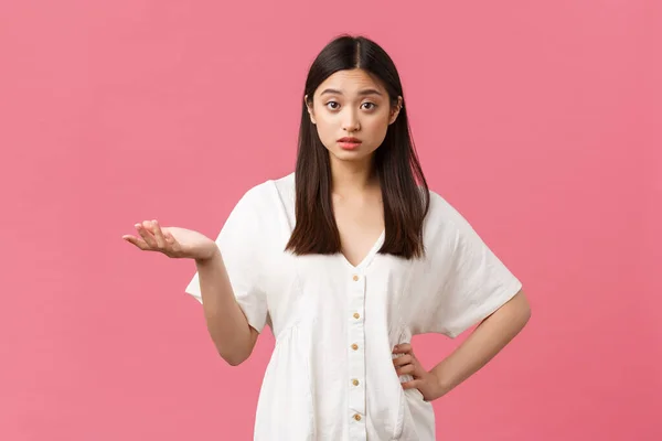 Szépség, emberek érzelmei és nyári szabadidő koncepció. Zavaros és zavaros ázsiai lány fehér ruhában, emelje fel a kezét, és vállat, nem érti, mit akarsz, rózsaszín háttér — Stock Fotó