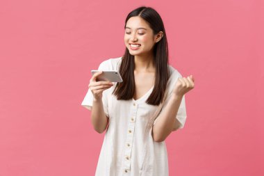 Güzellik, insan duyguları ve teknoloji konsepti. Neşeli mutlu kız oyunda kazanır, zafer kazanır ve gülümser. Cep telefonu ekranına bakarak tatmin olur, oyuncu kazanır ve kutlar, pembe arka plan.