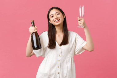 Kutlama, parti tatili ve eğlence konsepti. Neşeli mutlu Asyalı kız kız kız arkadaşlarıyla eğlenmeye hazır şampanya ve gözlük, gülümseyen kamera, neşeli pembe arka plan