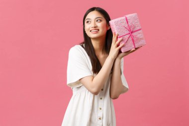 Kutlama, parti tatili ve eğlence konsepti. Beyaz elbiseli, mutlu, mutlu, gülümseyen beyaz elbiseli, doğum günü hediyesinin içinde ne olduğunu merak eden bir kadın.