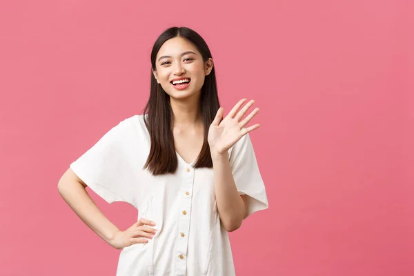 Krása, emoce lidí a letní volný čas. Přátelský a odcházející hezká asijská dívka v bílých šatech pozdravuje, mává rukou a veselý úsměv, pozdravuje někoho ahoj gesto — Stock fotografie