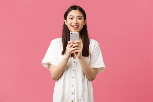Ομορφιά, ανθρώπινα συναισθήματα και τεχνολογική αντίληψη. Χαμογελώντας ευτυχισμένη Ασιάτισσα blogger, κομψή κοπέλα φωτογραφίζει στο smartphone, δείχνοντας αισιόδοξη ως φωτογράφηση, φωτογραφίζοντας με κινητό τηλέφωνο — Φωτογραφία Αρχείου