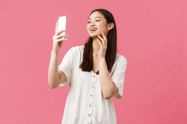 Piękno, ludzie emocje i koncepcja technologii. Kobiecy przystojny stylowy azjatycki dziewczyna blogger robi selfie na smartfonie aparat, uśmiechnięty szczęśliwy na telefon komórkowy, stojący różowy tło — Zdjęcie stockowe