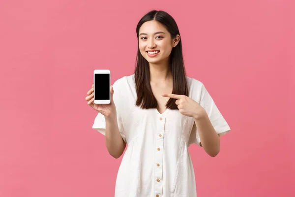 Bellezza, emozioni delle persone e concetto tecnologico. Ragazza coreana piuttosto elegante che mostra l'applicazione sullo schermo dello smartphone. Donna promuovere negozio o app, puntando il dito verso il telefono cellulare e sorridendo — Foto Stock