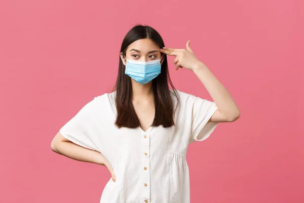 Covid-19, social distancing, virus and lifestyle concept. Annoyed and distressed asian female student in medical mask, showing fake gun over temple as killing herself from boredom or annoyance — Stock Photo, Image