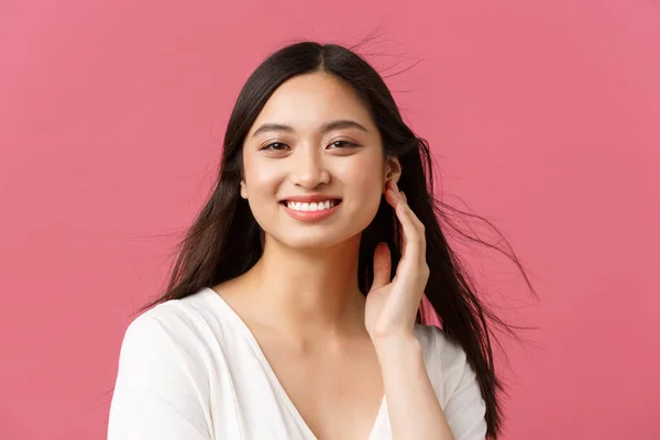 Salão de beleza, cabeleireiro e produtos para a pele conceito de propaganda. Close-up de bela jovem mulher asiática sorrindo como vento suavemente soprando no corte de cabelo, de pé fundo rosa — Fotografia de Stock