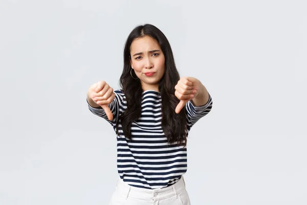 Lifestyle, beauty and fashion, people emotions concept. Judgemental disappointed asian woman showing negative opinion, make thumbs-down and smirk unsatisfied, rating bad product — Stock Photo, Image