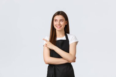 Küçük işletmeler, çalışanlar ve kahve dükkanı konsepti. Siyah önlüklü, mutlu ve çekici bir bayan tezgahtar solu işaret ediyor ve reklamlara bakıyor. Neşeli barmen harika bir reklam buldu.