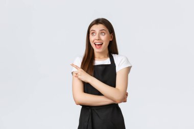 Küçük işletmeler, çalışanlar ve kahve dükkanı konsepti. Heyecanlı, mutlu ve gülümseyen kafe çalışanı şaşırmış ve solu işaret ediyor. Etkileyici bir mağaza çalışanı havalı reklamlara tepki veriyor.