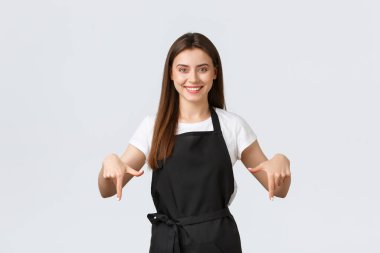 Küçük işletmeler, çalışanlar ve kahve dükkanı konsepti. Marketteki gülümseyen çekici tezgahtar kadın parmaklarını aşağı işaret ediyor. Şirin kafe çalışanı müşterilere özel satış bilgileri sağlıyor