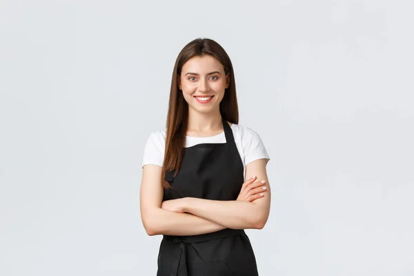 Allegro sorridente barista donna in grembiule nero petto braccia incrociate, cercando pronto e sicuro di sé. Ragazza dipendente aprire caffetteria, salutare i clienti. Commerciante negozio di corsa — Foto Stock