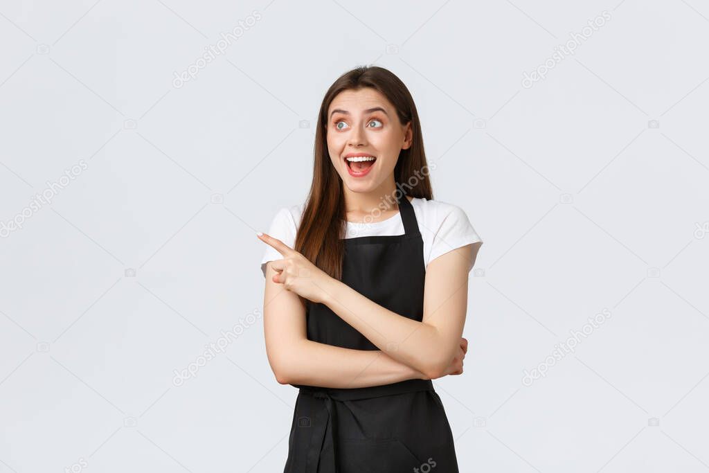 Small business, employees and coffee shop concept. Excited happy and smiling cafe worker looking astonished and pointing left. Impressed cute store employee react to cool advertisement
