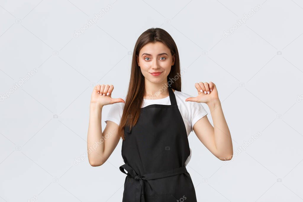 Small business, employees and coffee shop concept. Confident good-looking female barista in black apron pointing at herself and smiling pleased, show-off, being best employee of month