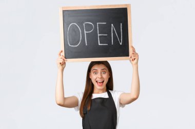 Market çalışanları, küçük işletmeler ve kahve dükkanları konsepti. Siyah önlüklü neşeli barista açık tabelayı kaldır, müşterilere salgın hastalıktan sonra dükkan ya da kafenin çalıştığını bildir.