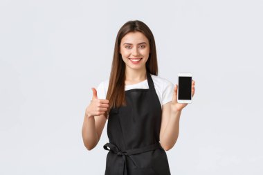 Market çalışanları, küçük işletmeler ve kahve dükkanları konsepti. Tatmin olmuş sevimli arkadaş canlısı barista ya da garson kız başparmaklarını göster ve cep telefonu sreen, uygulama indirmeyi tavsiye et