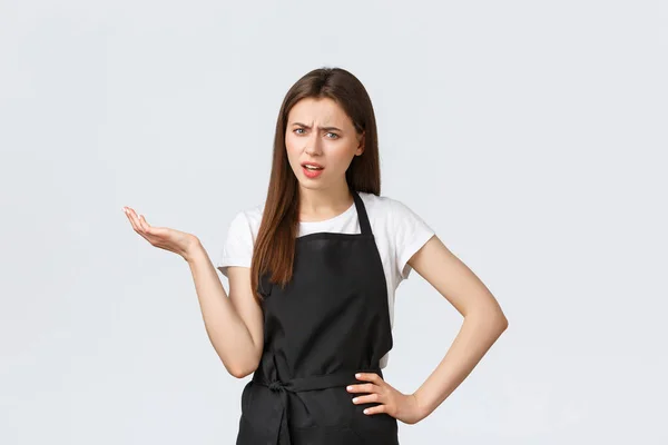 Grocery store employees, small business and coffee shops concept. Annoyed skeptical female barista in black apron saying so what. Saleswoman raise hand in dismay looking bothered — Stock Photo, Image