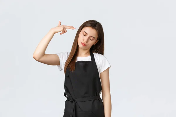 Grocery store employees, small business and coffee shops concept. Annoyed and tired saleswoman in black apron pointing fake gun at head irritated, staring skeptical and bothered — Stock Photo, Image