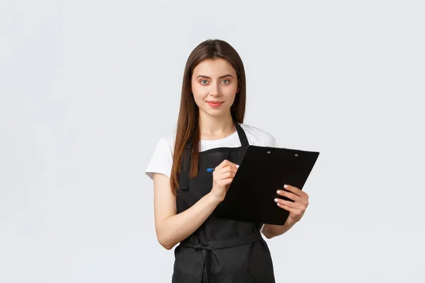 Empregados de mercearia, conceito de pequenas empresas e cafés. Gerente de loja verificando produtos em estoque, escrevendo itens na área de transferência, vestindo uniforme de avental preto, fundo branco — Fotografia de Stock