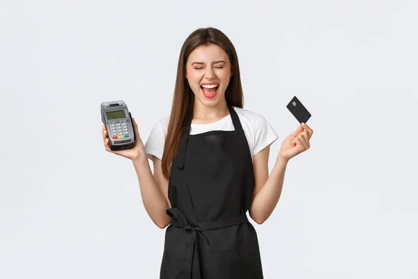 Grocery store employees, small business and coffee shops concept. Smiling carefree cashier close eyes and grinning joyful while standing with POS terminal and credit card, white background
