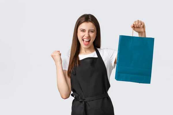 Mitarbeiter im Lebensmittelgeschäft, Kleinunternehmen und Coffeeshops. Jubelnde Verkäuferin in schwarzer Schürze zeigt Papier mit Kundenauftrag und Faust im Triumph — Stockfoto