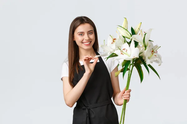 Einkaufen, Mitarbeiter und Kleinunternehmerkonzept. Lächelnd hübsche Verkäuferin Floristin im Blumenladen hält Strauß weißer Lilien und lächelt, bereiten Bestellung für Kunden — Stockfoto