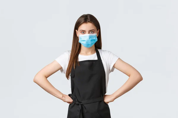 Covid-19 social distancing, cafe employees, coffee shops and coronavirus concept. Manager in grocery store standing bossy with hands on waist, wearing medical mask, follow preventing virus protocol