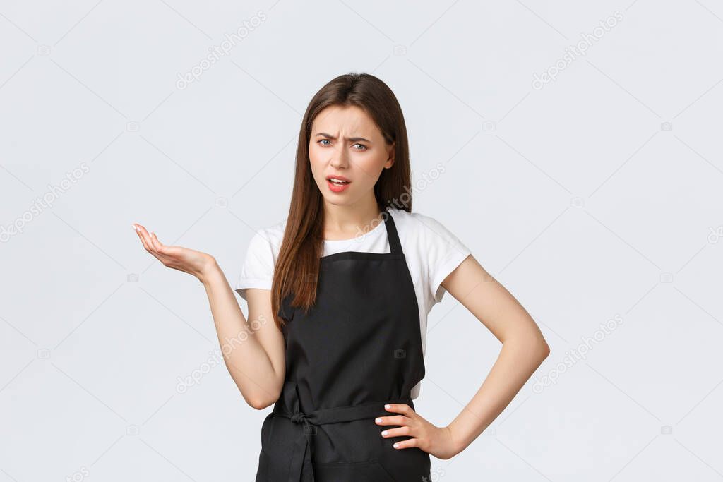 Grocery store employees, small business and coffee shops concept. Annoyed skeptical female barista in black apron saying so what. Saleswoman raise hand in dismay looking bothered