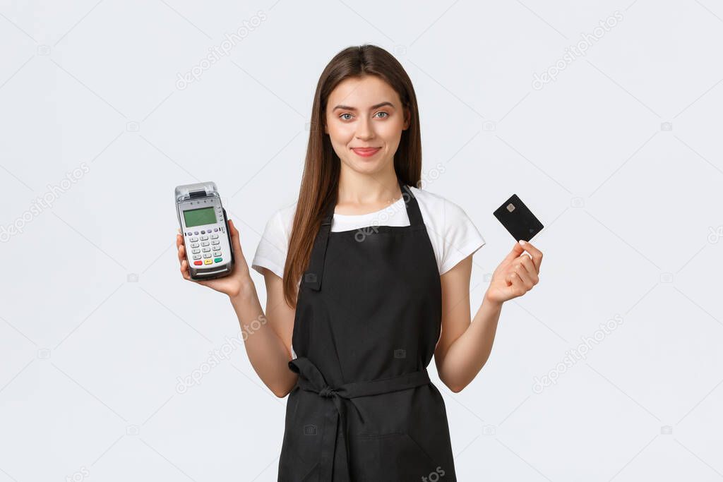 Grocery store employees, small business and coffee shops concept. Helpful cute cashier in black apron showing credit card and payment terminal POS, help guest pay for order