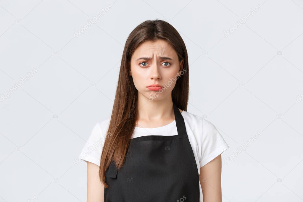 Employees, job employment, small business and coffee shop concept. Gloomy disappointed female barista, cashier in black apron frowning uneasy, pouting troubled over white background