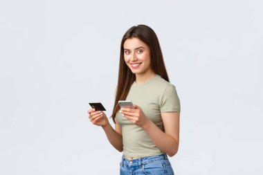 Çevrimiçi alışveriş, ev hayatı ve insan konsepti. Günlük kıyafetlerle gülümseyen çekici bir kadın akıllı telefonuyla uçuş rezervasyonu, teslimat için kredi kartı ve cep telefonu, yer siparişi