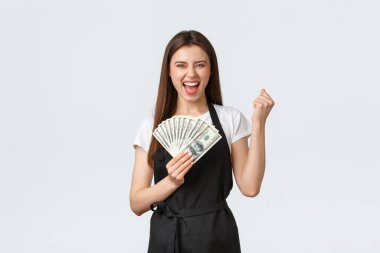 Market çalışanları, küçük işletmeler ve kahve dükkanları konsepti. Kafe çalışanı olarak ilk maaş çekini kutlayan mutlu bir barmen. Yumruk tokuşturma ve para gösterme. Neşeli gülümseme.