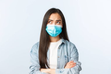Sosyal mesafeli yaşam tarzı, covid-19 salgını günlük yaşam ve eğlence kavramı. Sağlık maskeli düşünceli Asyalı kız sol üst köşeye bakıyor, düşünüyor, endişeleniyor.