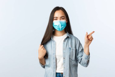 Sosyal mesafeli yaşam tarzı, covid-19 salgını günlük yaşam ve eğlence kavramı. Mutlu Asyalı kız saçlarına dokunuyor, yeni bir saç kesimi yaptırıyor, güzellik salonu reklamını işaret ediyor.