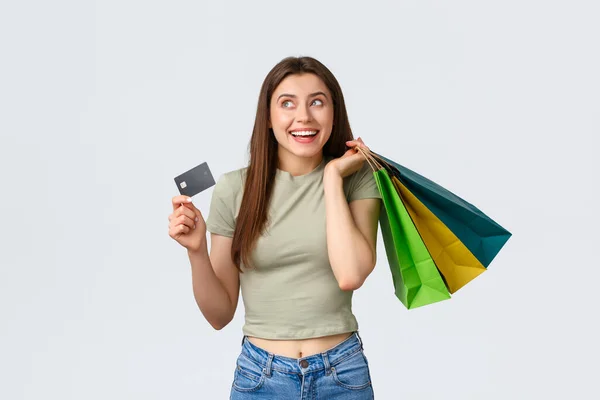 Shopping center, estilo de vida e conceito de moda. Sonhador mulher elegante de boa aparência com cartão de crédito e sacos de loja, pensando em férias perfeitas em novas roupas que ela comprou — Fotografia de Stock