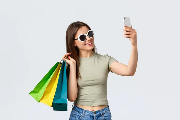 Shopping center, estilo de vida, turismo e conceito de moda. Feliz mulher atraente turista em óculos de sol posando com sacos de compras como tirar selfie, comprar coisas em lojas favoritas — Fotografia de Stock